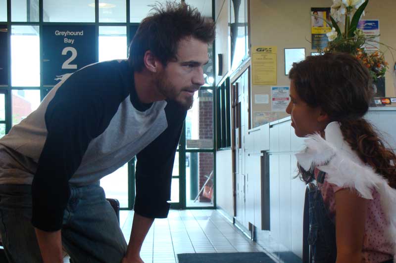 Man at bus stop talks to young girl wearing angel wings