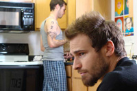 Man sits in kitchen while roommate cooks