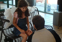 Young girl wearing angel wings sits on a bench at a bus stop